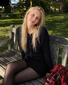 Ксения Волкова сидит на деревянной скамейке в парке
